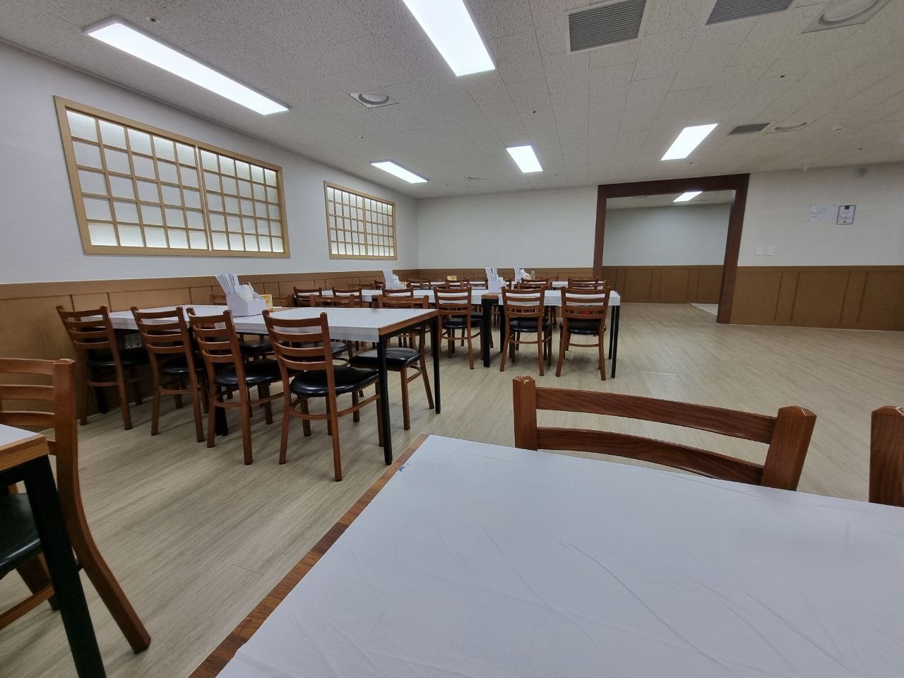 용인제일메디장례식장 식사 공간과 목재 의자 장례식장 식사 공간에 테이블과 의자가 놓여 있다.